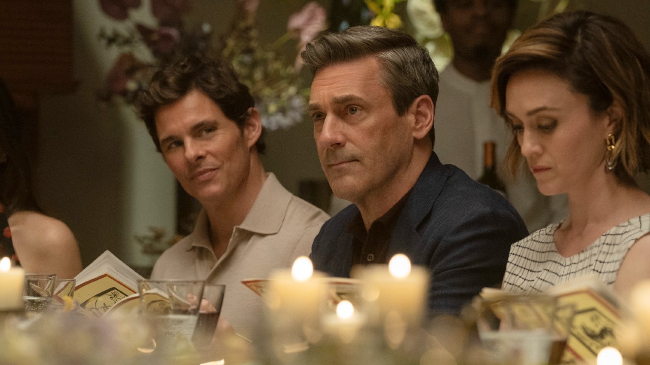 From left to right: James Marsden sitting at a table and looking to his right at Jon Hamm who is sitting right next to him. 