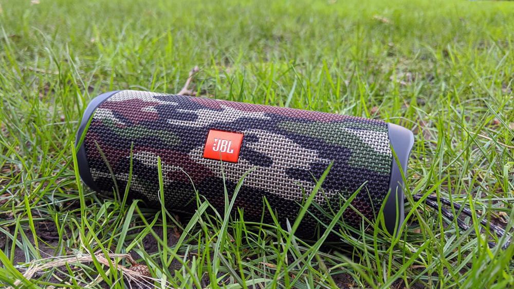 En vanntett høyttaler av typen JBL Flip 5 som ligger i gresset.