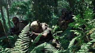 An armed soldier crouches in the Southeast Asian jungle.