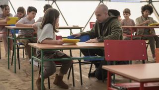 A man kneels before a little girl in a classroom