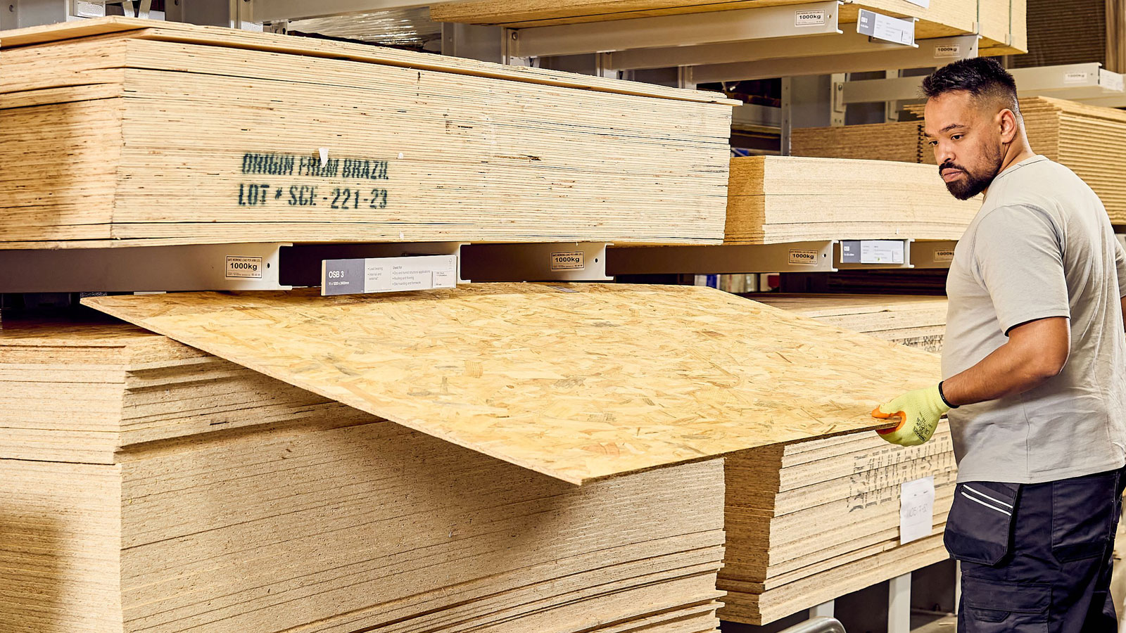 Person taking a sheet of OSB off top of pile in warehouse