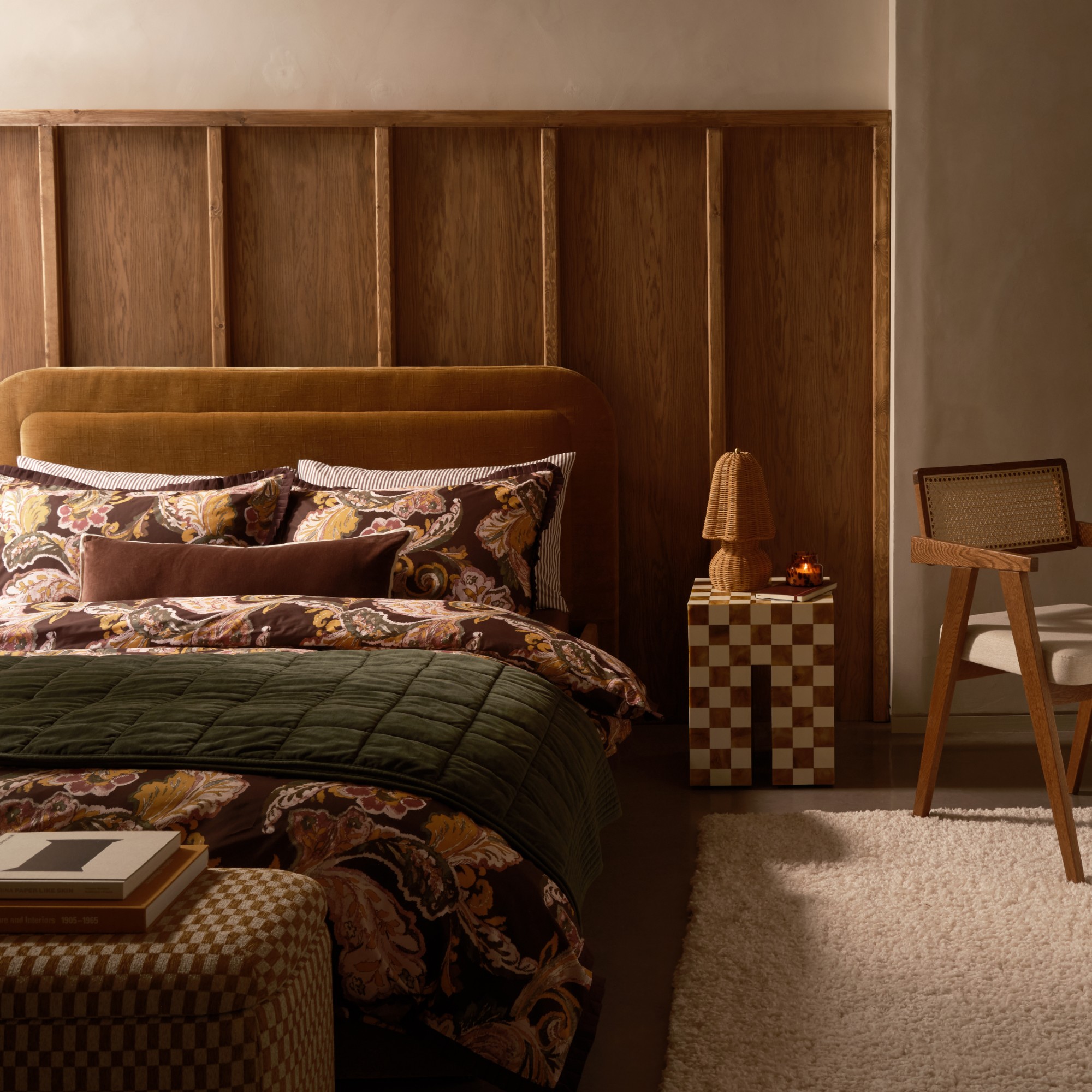 A bedroom with an upholstered headboard in caramel velvet, a dark green throw and brown floral bedding