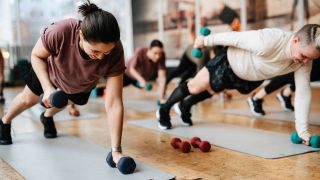 Women perform renegade row exercise using dumbbells in a studio