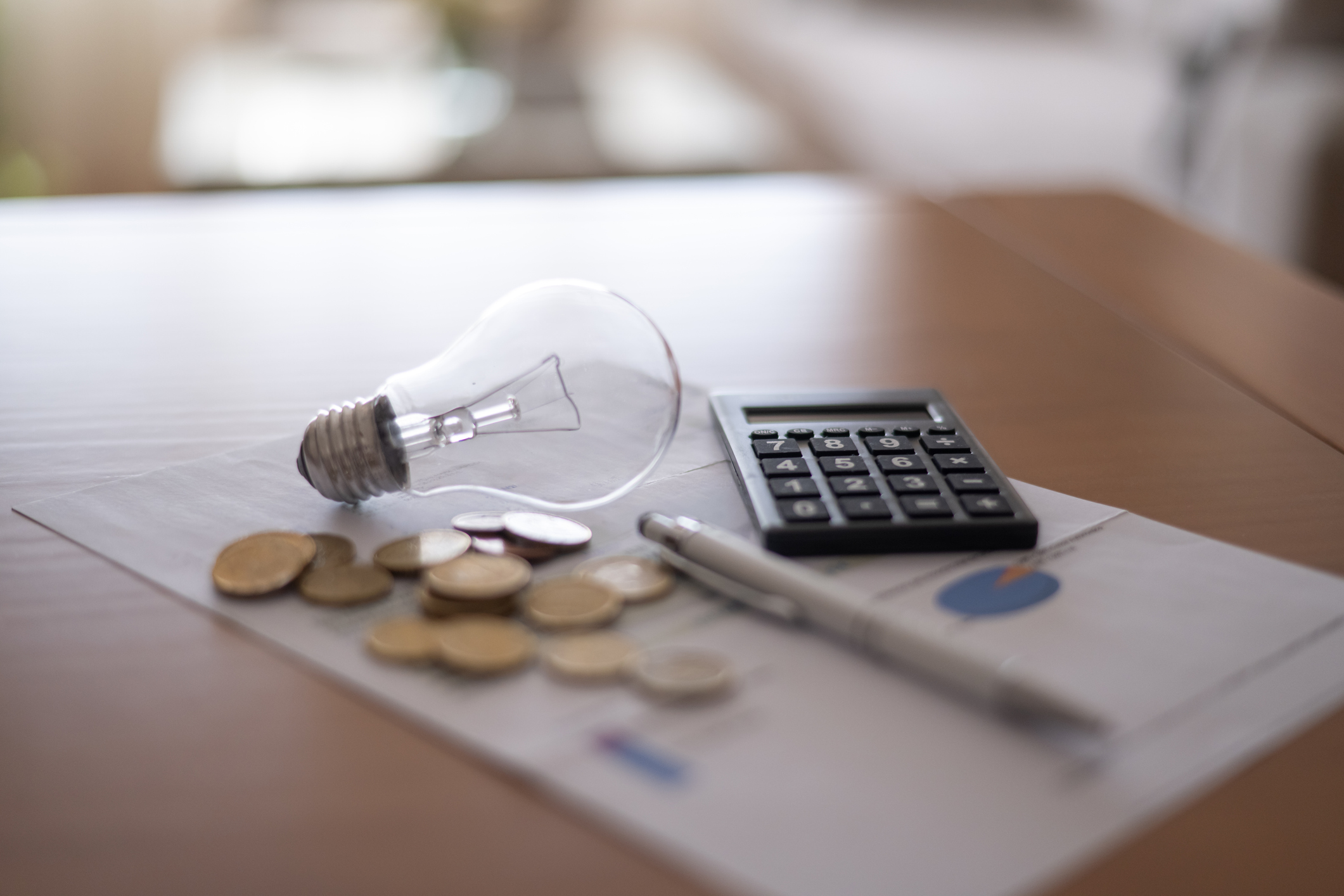 Light bulb, calculator, pen and coins sitting on financial documents, representing rising electricity prices, household expenses, and tax payment calculations