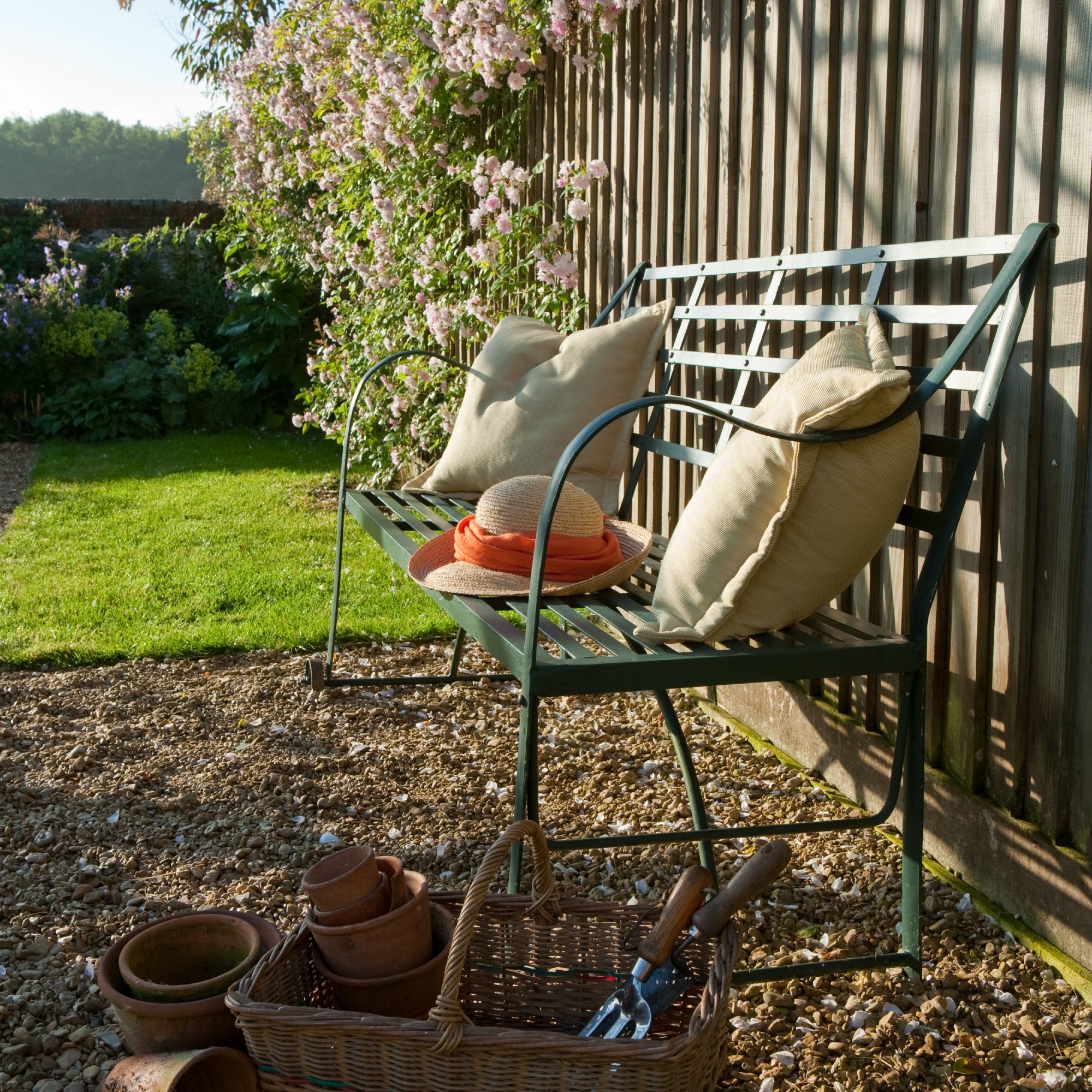 A garden with a green metal bench decorated with two yellow cushions