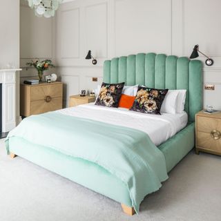 Bed with blue bed frame and headboard and decorative cushions, light oak bedside tables