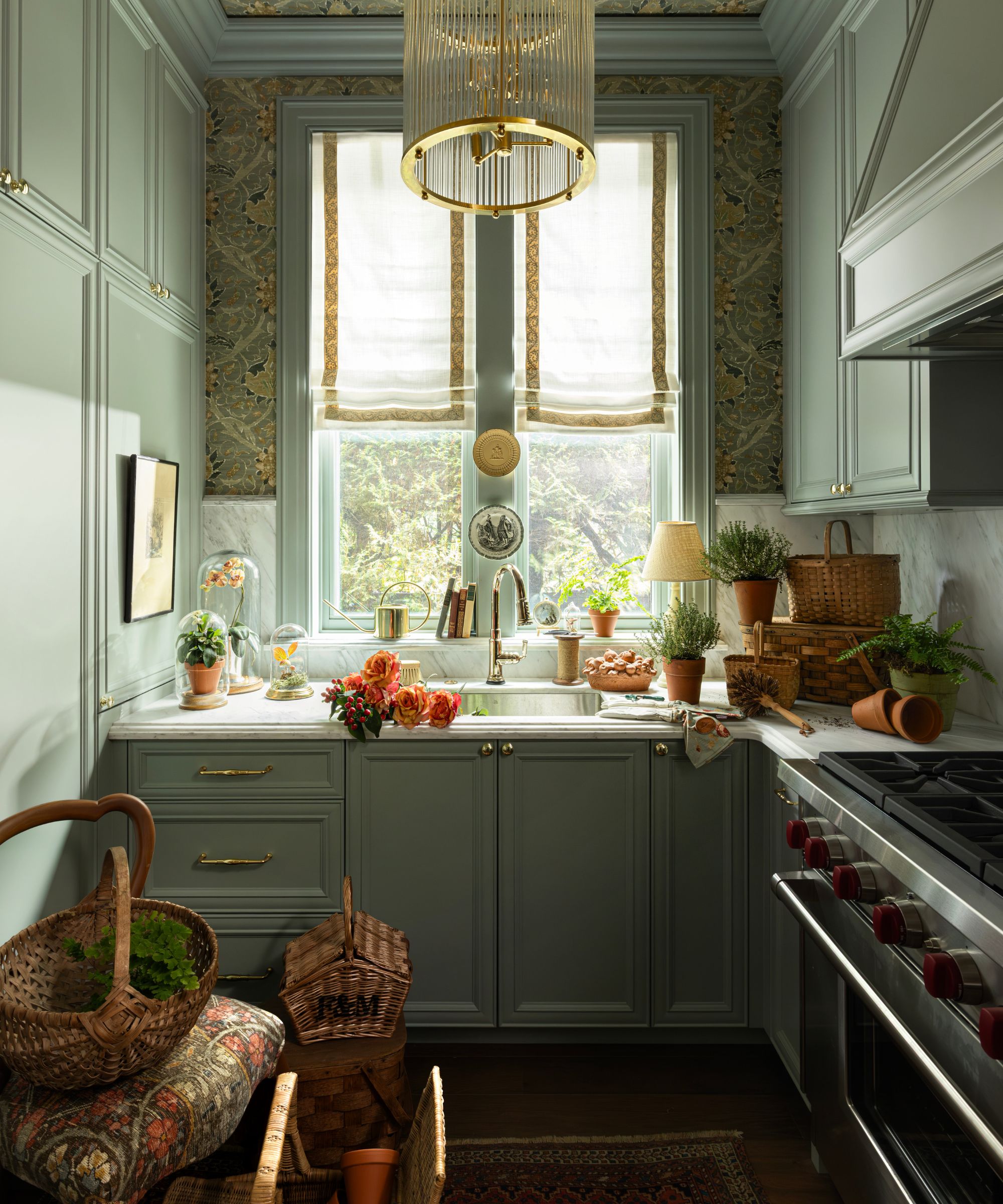 a soft green pantry with floral wallpaper on the ceiling, a window dressed with linen blinds and lots of potted plants and flowers decorating the countertop and window