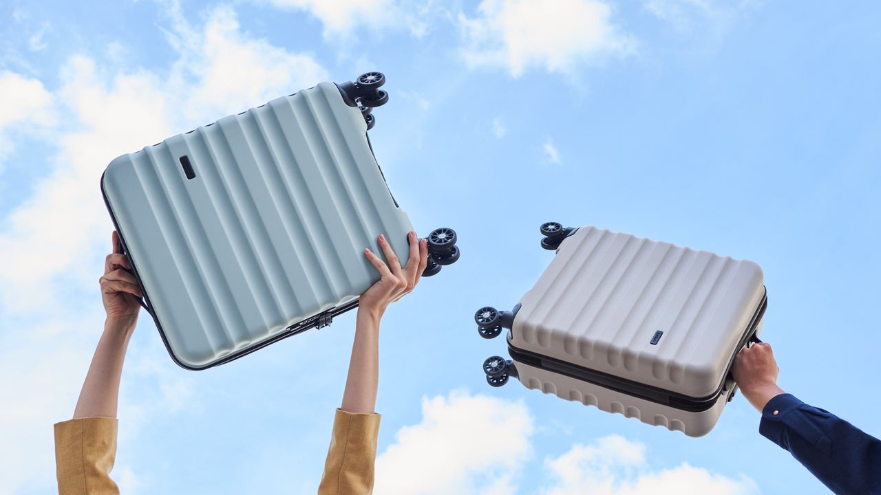 Two people holding two of the best carry-on luggage cases in the air, one case is baby blue and one is white