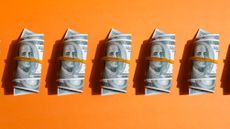 5 bundles of one hundred dollar bills wrapped in elastic bands on orange background 