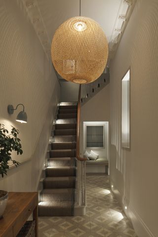 Hallway and staircase with pendant, wall and low level lighting and patterned floor tile