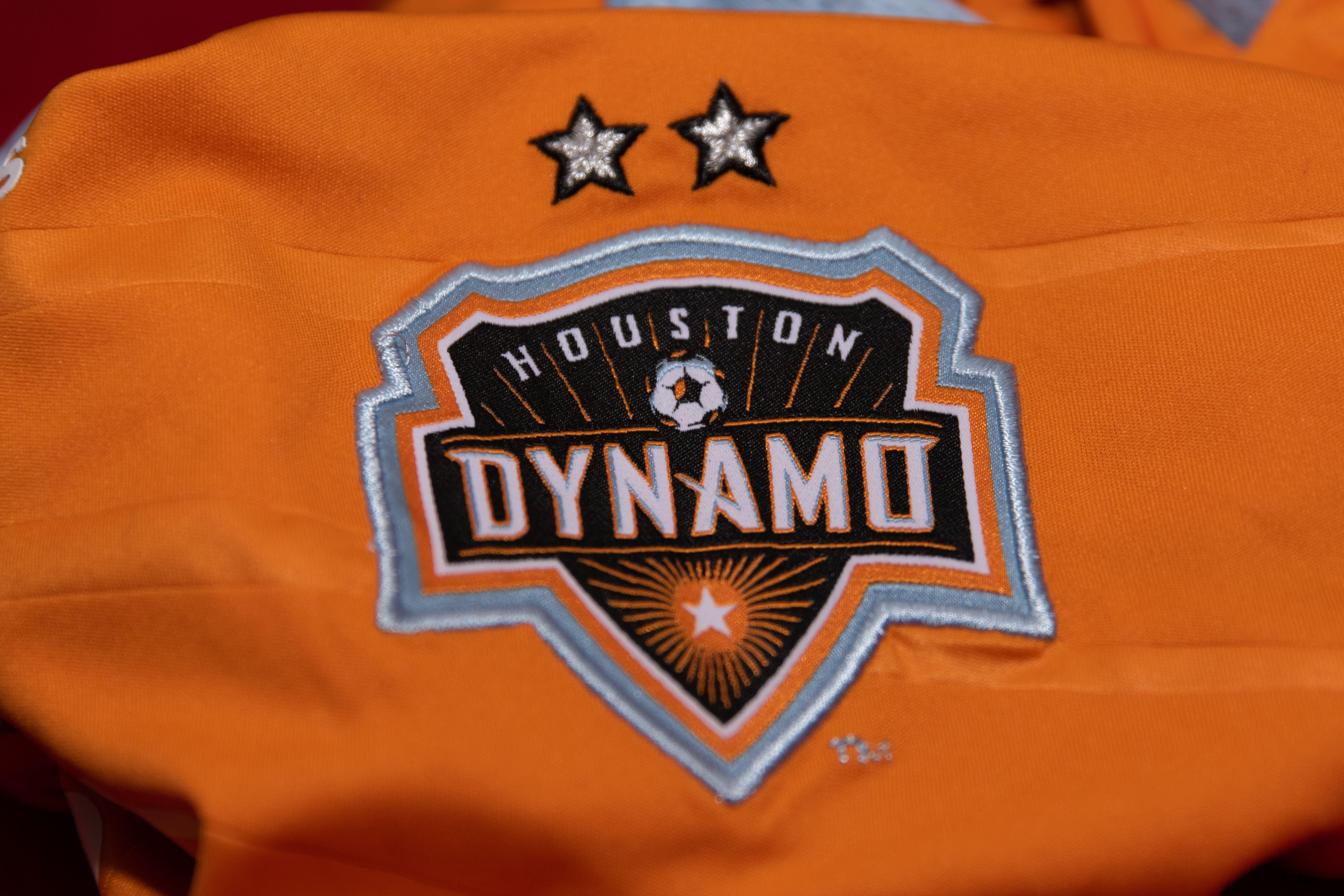 A close-up of the Houston Dynamo badge on an orange home shirt