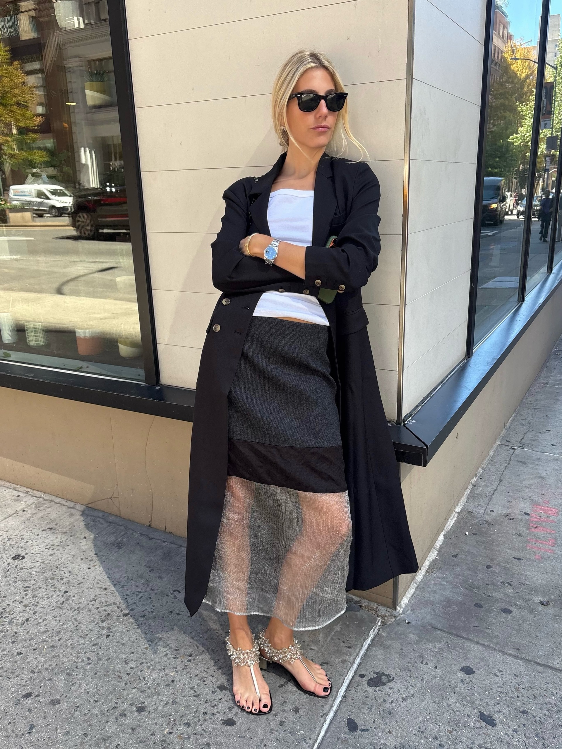 An image of an influencer in New York City wearing a sheer skirt with a long black coat and white top.