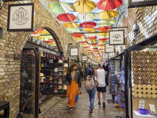 Shoppers stroll through Camden Market under an art installation of colorful, open parasols