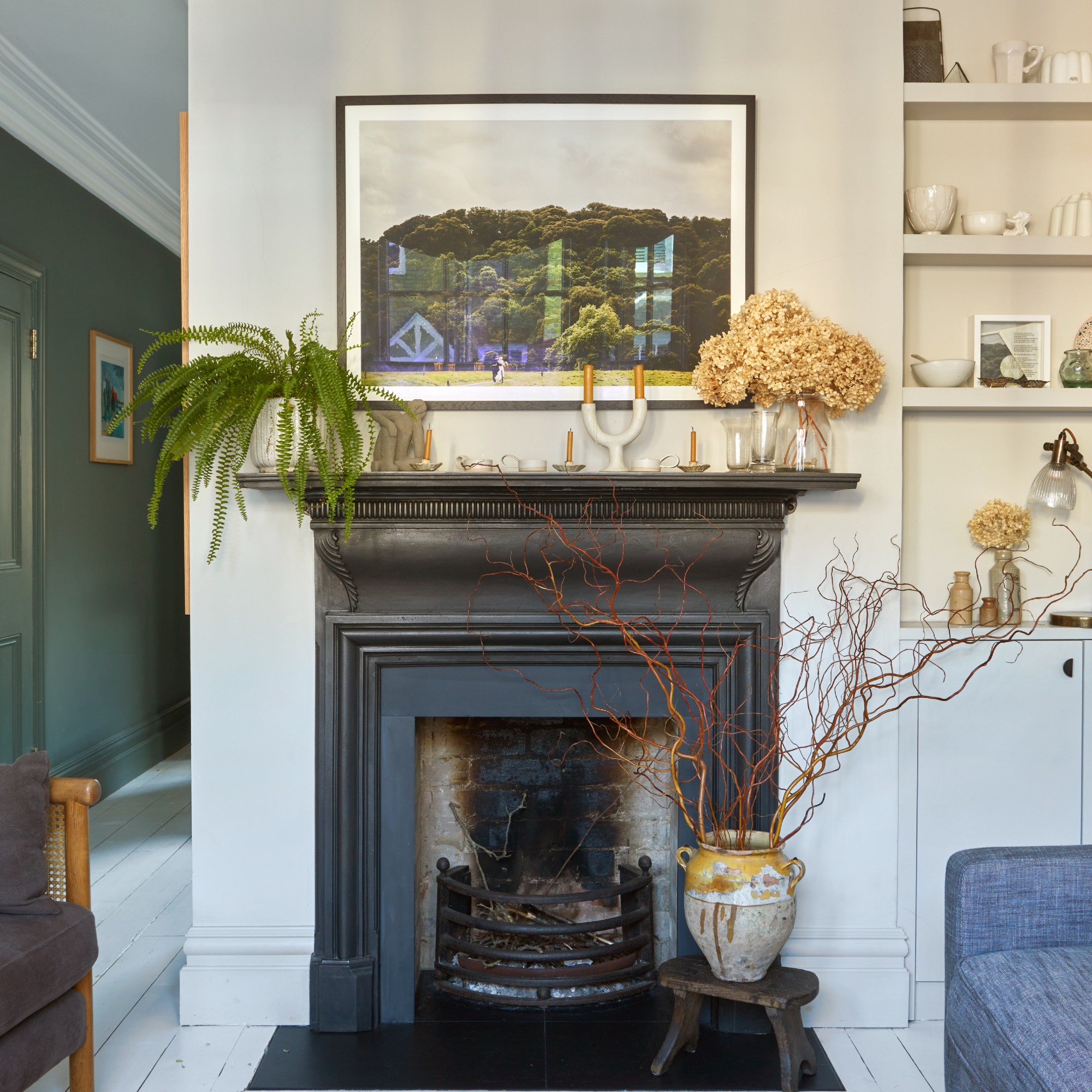 A living room with a black fireplace decorated with candleholders, flowers, plants and branches arranged in a vase