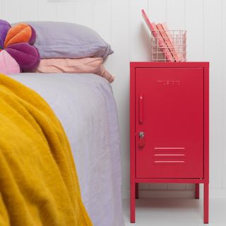 A bright pink locker next to a bed with a lilac duvet and mustard throw