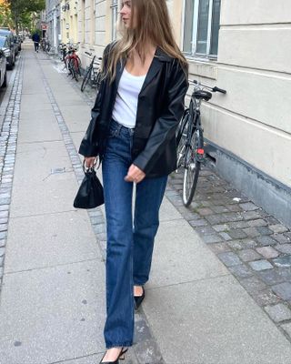 Scandinavian fashion creative influencer Clara Dyrhauge wears a black leather blazer, white tee, straight-leg jeans, mini black bag, and black slingback heels.