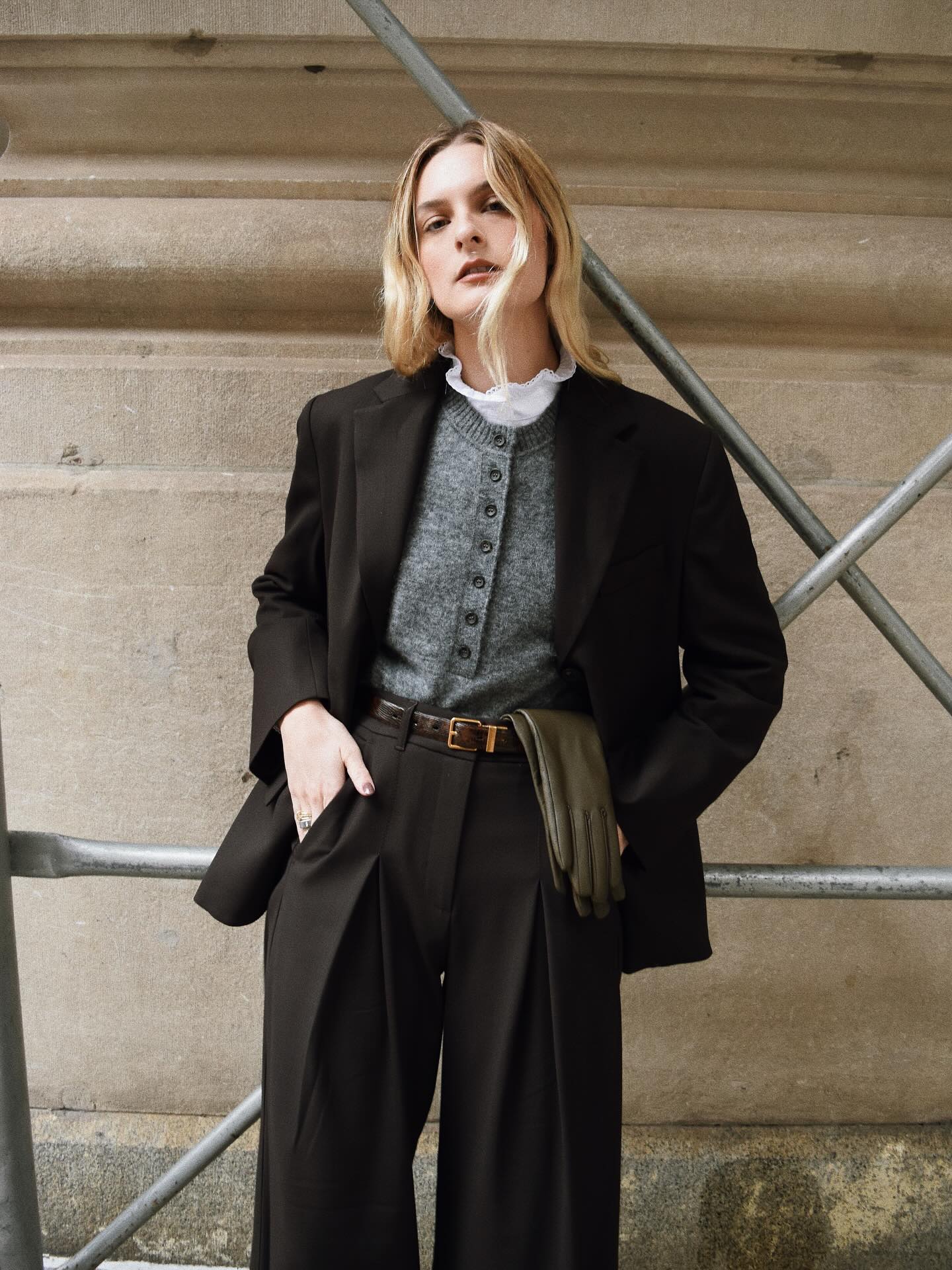An image of @christietyler wearing a frill neck blouse, grey cardigan, black blazer, black trousers and wrist-length gloves.