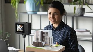 A woman presenting a miniature building in front of the Acer SpatialLabs Eyes Camera on a tripod.