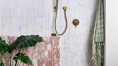 A bathroom with a gold shower, pink marble tiling, a green towel, and a large green leafy plant