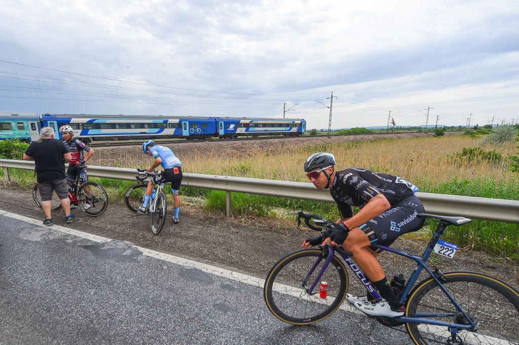 NYIREGYHAZA HUNGARY MAY 13 LR Carolina Upegui of Colombia and Team Bizkaia Durango Eri Yonamine of Japan and Team Human Powered Health and Emil Dima of Romania and Team Giotti Victoria Savini stopped due to a train crossing during the 43rd Tour de Hongrie 2022 Stage 3 a 154km stage from Sarospatak to Nyiregyhaza tourdehongrie on May 13 2022 in Nyiregyhaza Hungary Photo by Dario BelingheriGetty Images