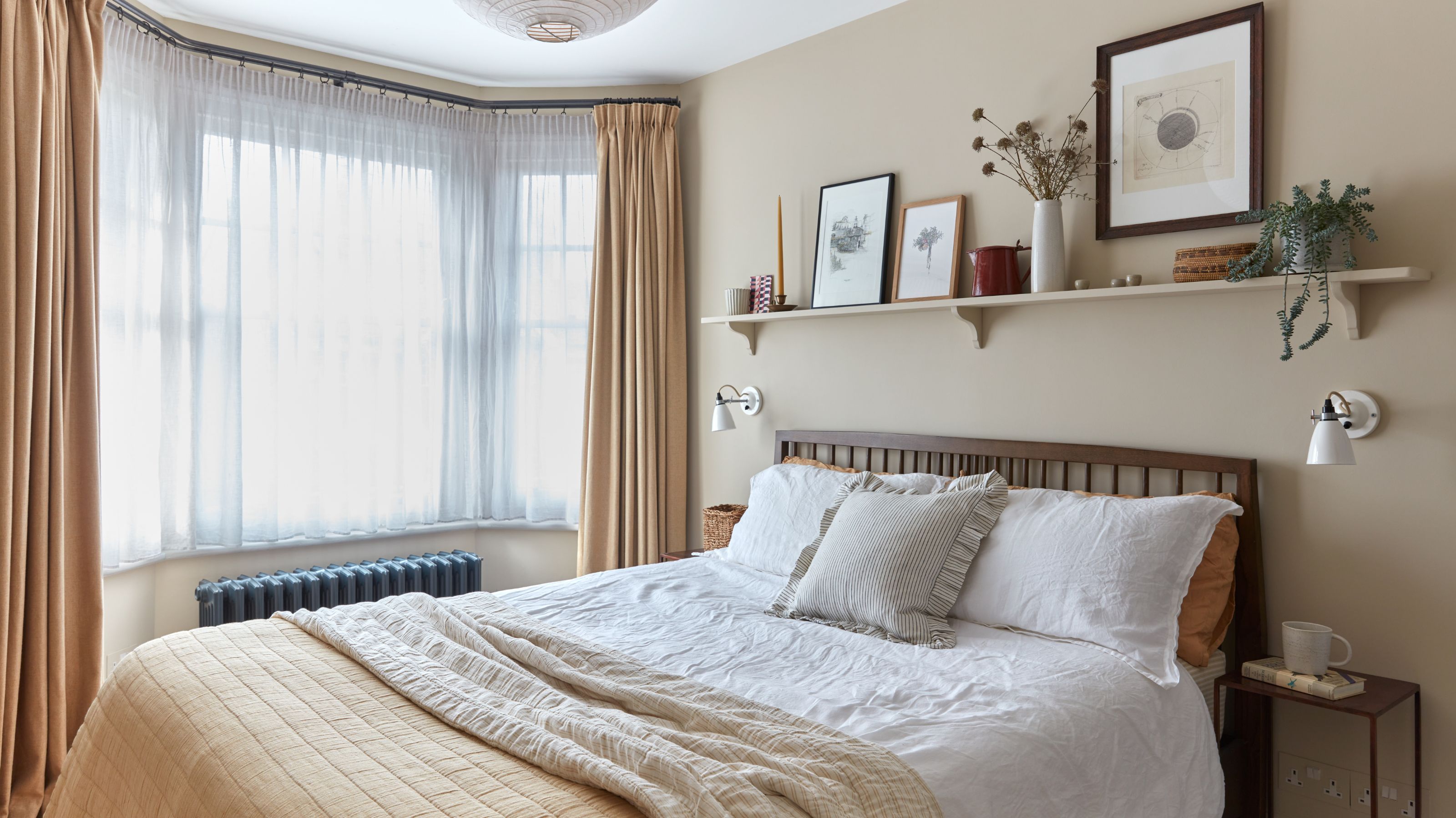 Neutral bedroom with beige walls and white bedding, with sheer curtains on the bay window
