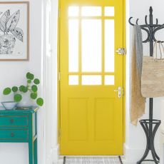 A hallway with a yellow front door, coat stand and a console table