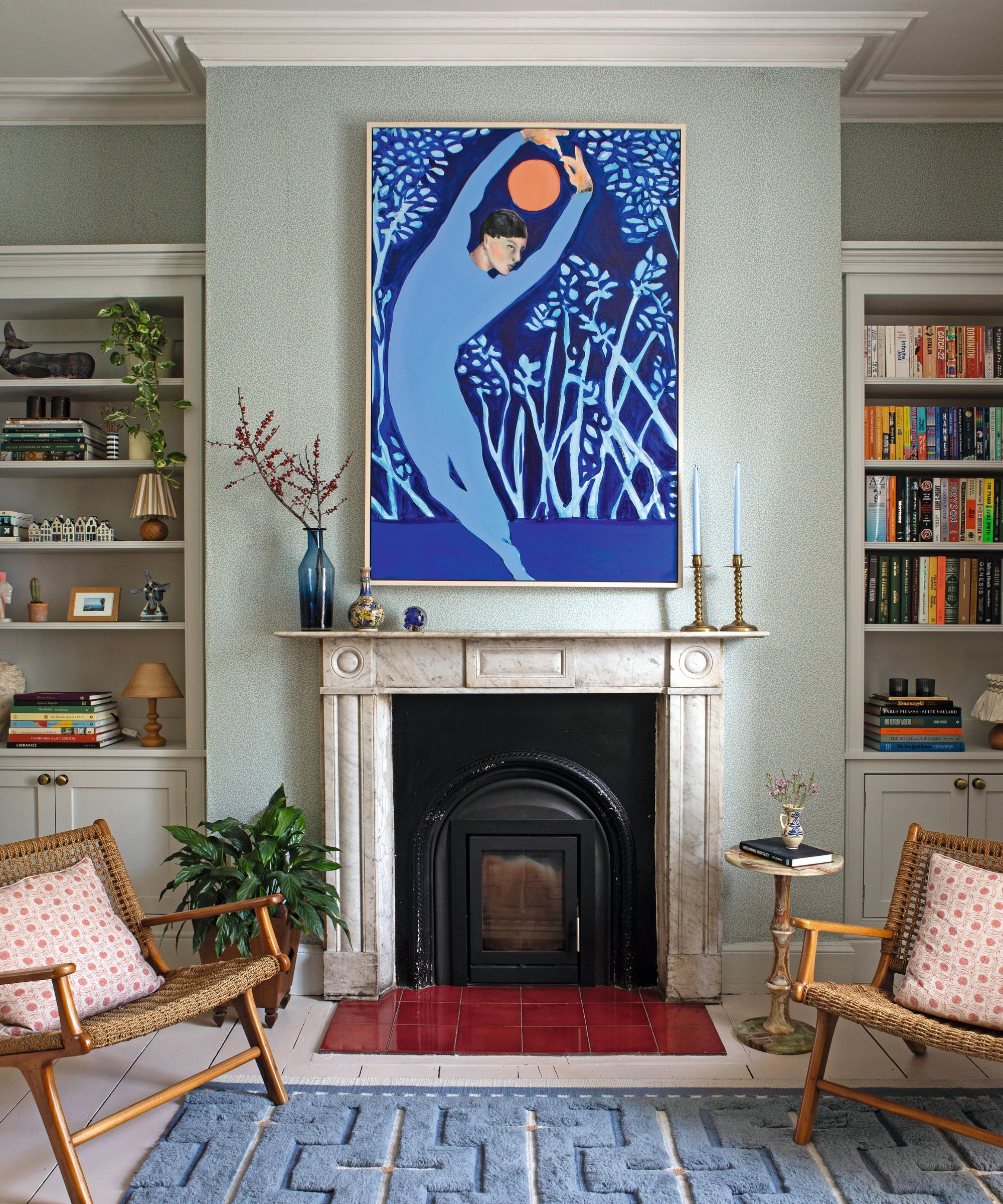 a pale blue green living room with a marble fireplace and statement art with bookcases either side