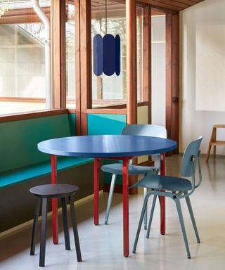 Blue and red dining table with colourful chairs and bright bench in a Scandinavian dining setting with wooden windows