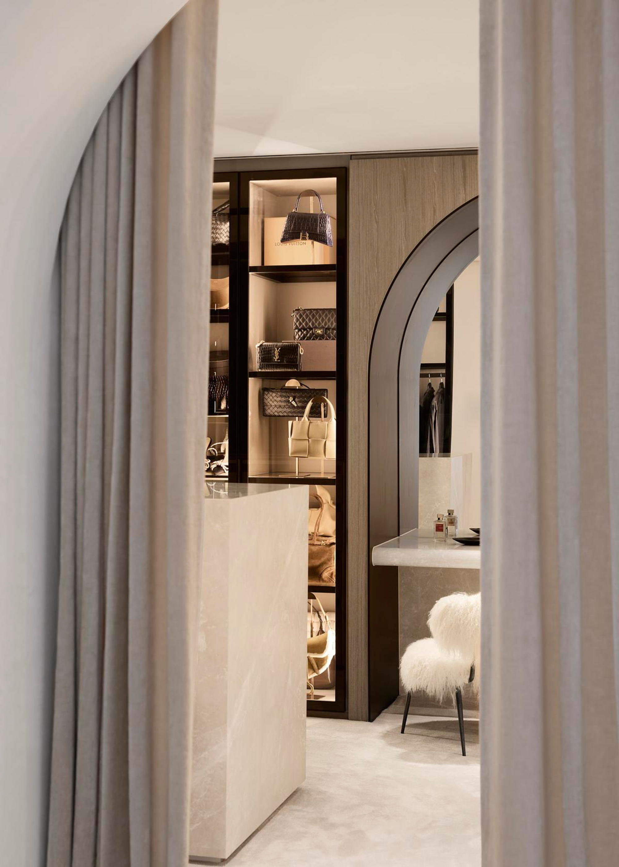 A white walk-in wardrobe with a dressing island, a vanity and cabinets with lighting