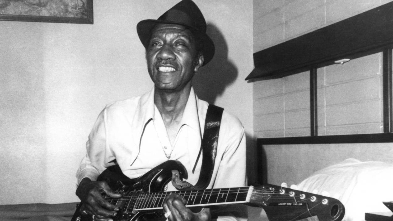 Hound Dog Taylor sitting on a bed and playing guitar