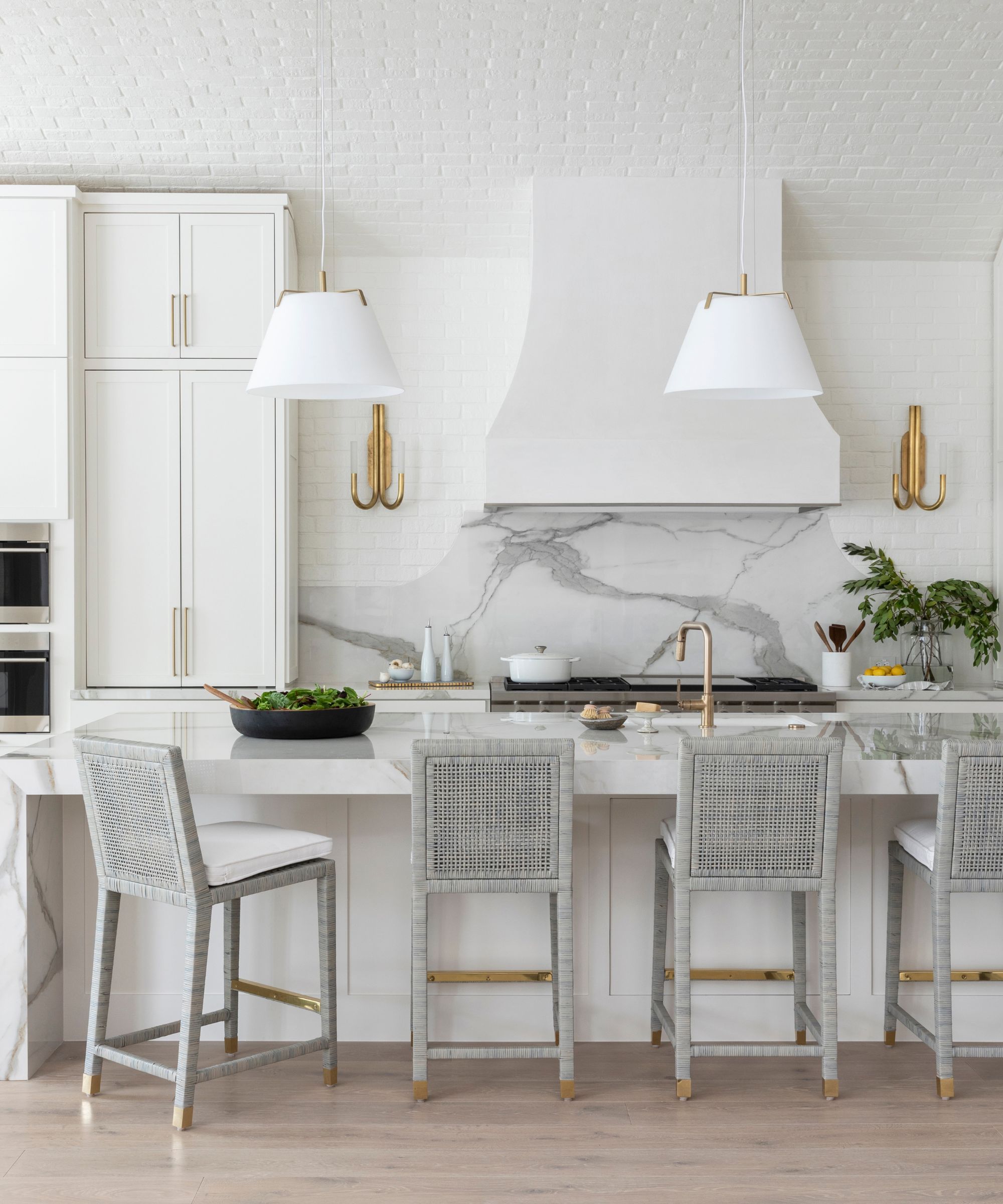A white kitchen with marble counters, a plaster range hood, and a layered lighting scheme