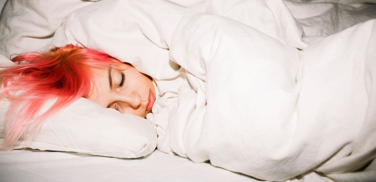 Young woman with pink hair sleeping soundly in bed