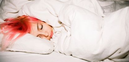 Young woman with pink hair sleeping soundly in bed