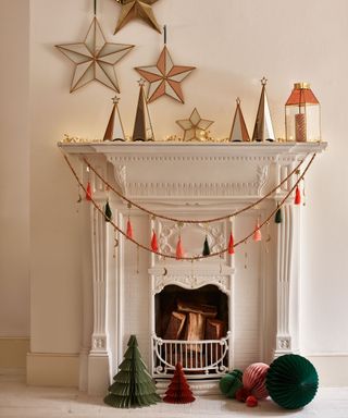 Playful festive fireplace styling with tassel garland, paper Christmas trees and mirrored star decorations