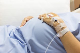 Image of a pregnant woman's belly and hand with an IV drip, in the hospital.