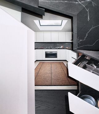 A collage of layered images featuring handle free white cupboards showing pans and cutlery. A long brown carpet laid, leading to the oven with a roof window above
