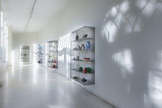 Wire cabinets by Muller Van Severen showing their contents, hanging on the wall of a sunlit corridor at Design Museum Ghent