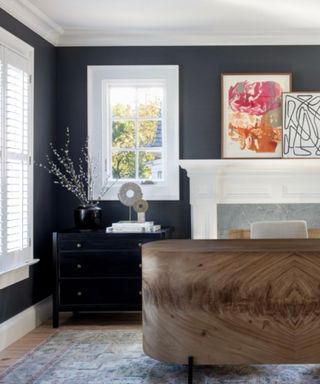 home office with black walls, large curved wooden desk and white fireplace