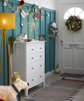 A hallway with blue wall panel decor, white chest of drawers, and Christmas card display