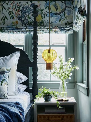 a blue bedroom with patterned curtains, a sculptural bed, a side table with plants, a floating yellow pendant light