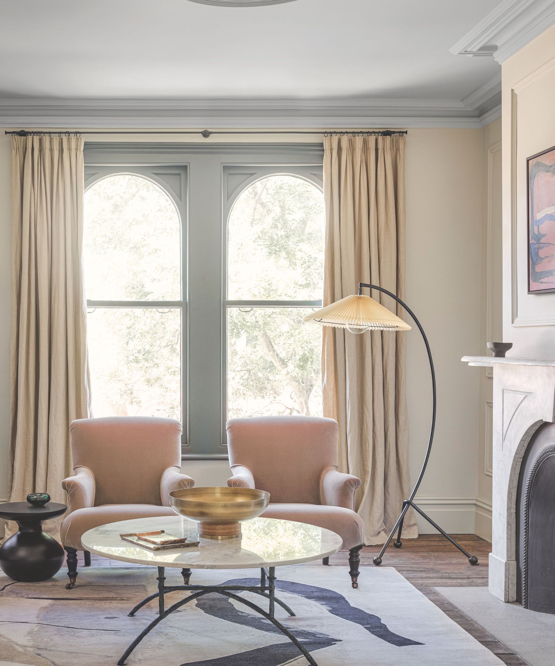 Living room with arched painted windows, two pink armchairs, marble coffee table and floor lamp