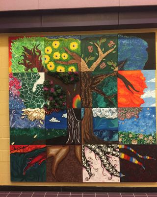 Colorful student-created patchwork style mural depicts a tree, field and sky.