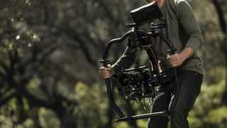 A man holding the DJI Ronin 2 camera gimbal out in the field
