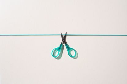 A small pair of green scissors opens to cut a green cord.