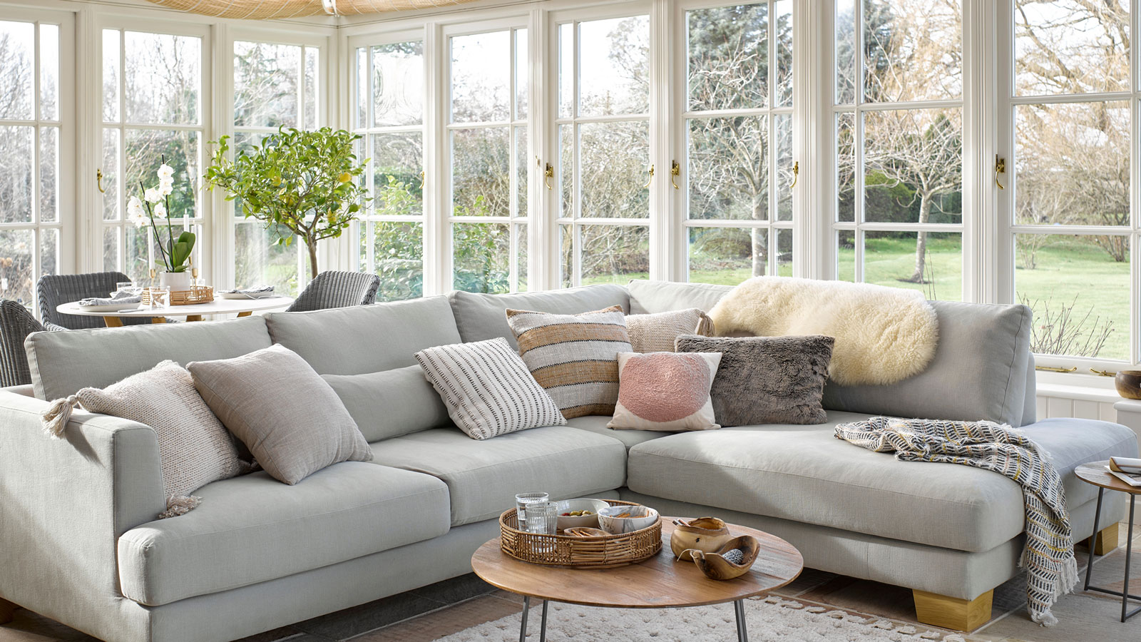 living room in a conservatory with large grey corner sofa and dining area