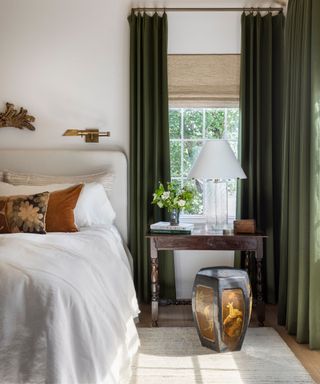 small neutral traditional bedroom with high dark green curtains with a small antique desk and stool