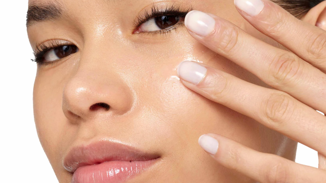 close up of woman&#039;s face with glowing skin brushing the 111SKIN repair serum onto her cheekbone