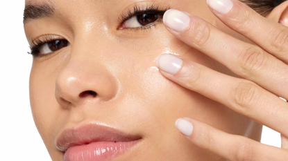 close up of woman's face with glowing skin brushing the 111SKIN repair serum onto her cheekbone