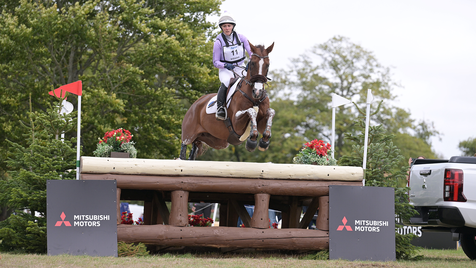 Gemma Stevens, a rider in a purple top and white hat, steers chestnut horse Chilli&amp;rsquo;s Jester, over a table fence with red flowers on top of it at Blenheim Horse Trials 2026