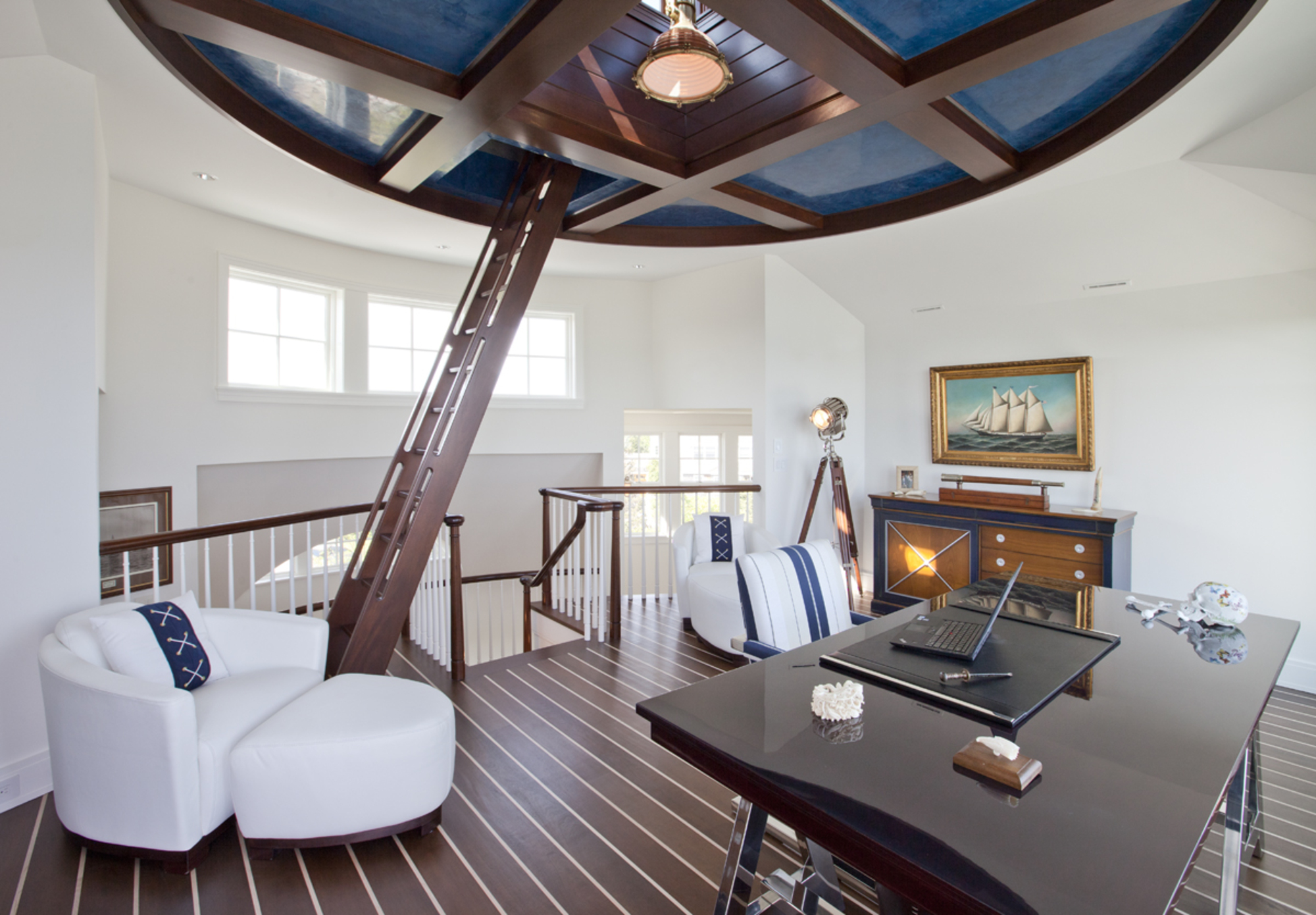 A home office on a mezzanine level with a wooden step ladder leading into a loft in a circular coffered ceiling